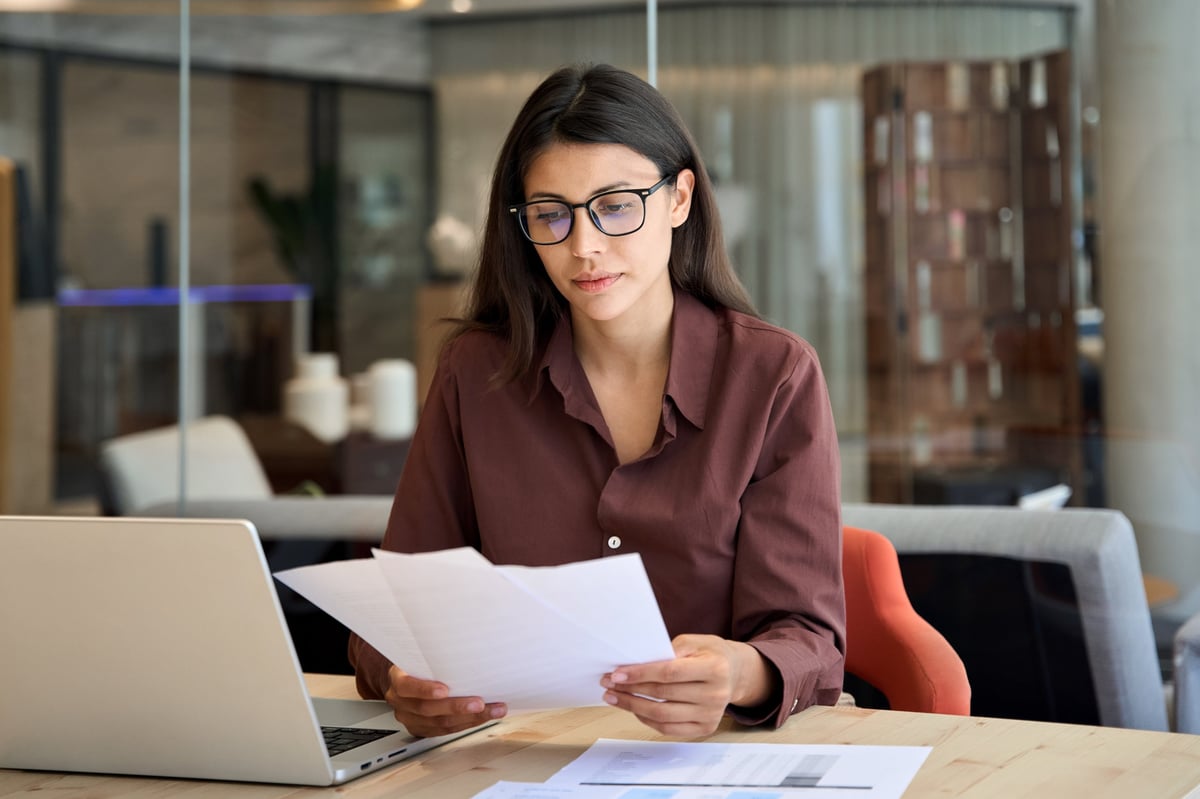 A focused businesswoman reviewing financial documents on a laptop